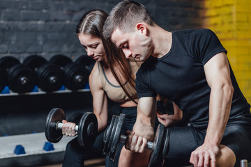 Fototapeta na wymiar Fitness, sports, exercises and weightlifting. Concept - a young woman and a young man with dumbbells sweeping muscles in the gym. During this time they look at their muscles.