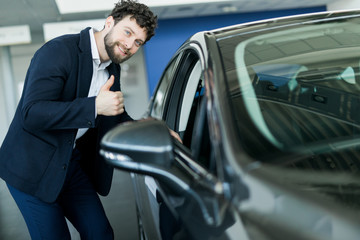 Fototapeta na wymiar Perfect car. Happy mature male buyer showing thumbs up leaning on his new car at the dealership
