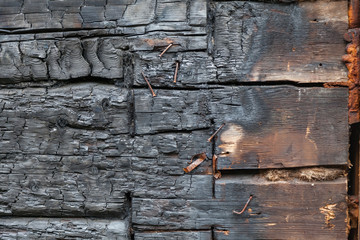 Background of a wall made of horizontal half-burned black boards in the form of coals with nails and self-tapping screws. Fire and extinguishing.