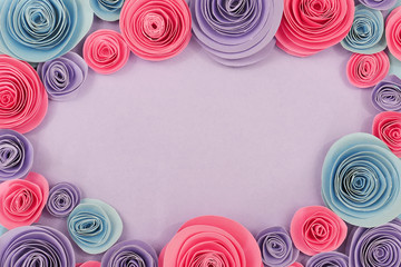 Pastel blue, pink and violet paper rose flat lay background with flowers around the endges and empty copy space in middle