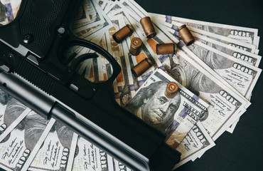 Gun with bullets lying on the table. Money on black background. Criminal problems. Dollars.