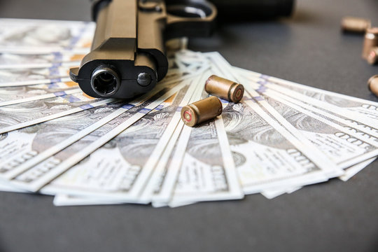 Gun with bullets lying on the table. Money on black background. Criminal problems. Dollars.