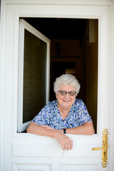 elderly senior woman opening front door of house and welcoming people at home