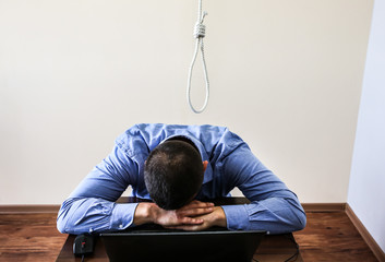 Noose is above the office worker. Suicide concept. Hanging because of work stress. Depression of burnout. Terrible life situation. Man near the laptop at the desk.