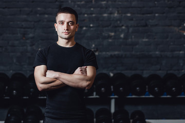 A young athlete is standing in the gym. During this dress, wear a black T-shirt. Standing on a black background and looking at the camera.