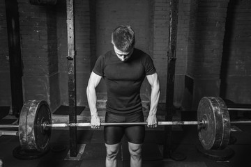 Fototapeta na wymiar Young athlete dressed in black t-shirt. During this time, he trains crossfit to the gym. At the same time, it raises the bar with maximum effort.