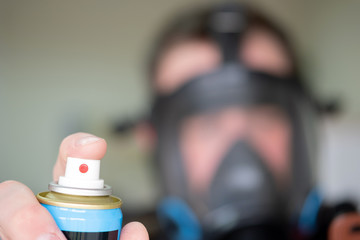 a can of gas in the foreground in the hand of a man the background of a man in a black gas mask blurred out of focus