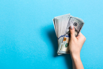 Top view of female hand holding a pack of one hundred dollar bills on colorful background. Wage and salary concept with empty space for your design