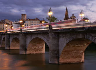 Fototapeta premium vistas del puente medieval, el río Ebro y la ciudad historica de Logroño en la Rioja,España, durante el anochecer, con estelas y reflejos de los vehiculos que transitaban el lugar