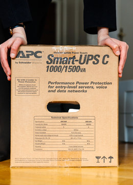 PARIS, FRANCE - MAR 29, 2018: IT woman unboxing APC Smart-UPS C 1000VA LCD 230V enterprise-level uninterruptible power supplies made by American Power Conversion office wooden floor