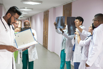 a team of young doctors. A group of people of different races, of different sexes, dressed in medical clothes, in the corridor of the hospital, looking at an x-ray, discussing medicine