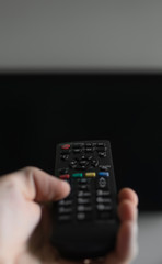 The man with the remote control in hand want switch on the TV and presses the button on the remote control. Remote control in hand closeup.