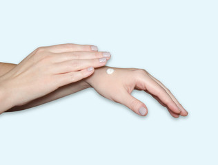 A woman's hands, a drop of white moisturizer on her arm. Hand care, skin hydration