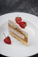 cake, a piece of delicate cake, with sliced fresh strawberries, on a white plate, on a white and gray abstract dark background. confectionery