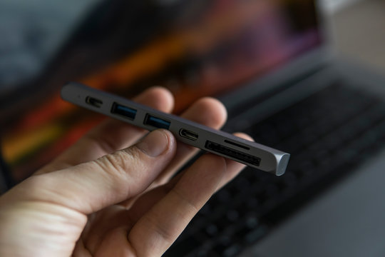 Man's hand holding The USB adapter under the Type-C connector for laptop. Multiport station for laptop with multiple different ports. USB to USB Type-C Hub Converter.
