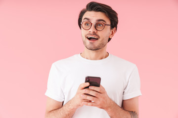 Image of unshaven smiling man wearing eyeglasses looking aside and using cellphone