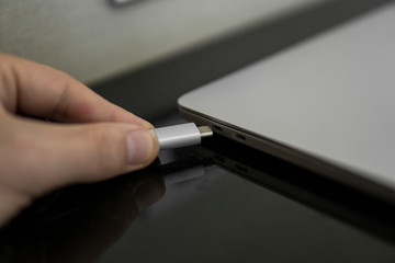 Male hand plugging white USB-C Type C cable into a port on a grey laptop notebook computer. USB type-C port and Cable's White of laptop.