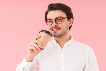 Image of caucasian joyful man wearing eyeglasses drinking coffee from paper cup and winking