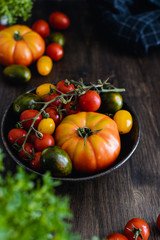 Colorful organic tomatoes in a bowl on dark wooden background