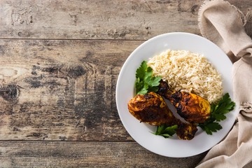 Roasted tandoori chicken with basmati rice in plate on wooden table. Top view. Copy space