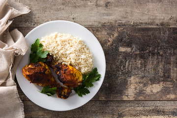 Roasted tandoori chicken with basmati rice in plate on wooden table. Top view. Copy space