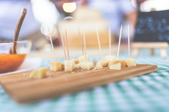 Close up of small cheese sample pieces with toothpicks on wooden cutting board.