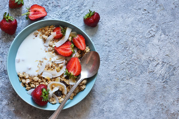 Classic breakfast - granola, coconut chips, Greek yogurt and strawberries in a beautiful plate on the kitchen table. View from above.