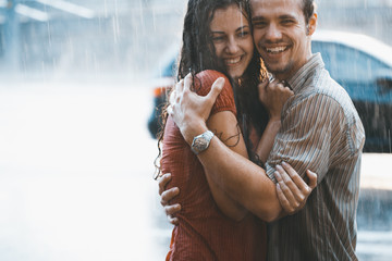 Couple in love hugging and kissing under he rain. They are wet and smiling