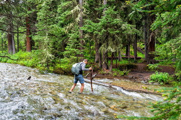 Man crossing river strong current ford on Conundrum Creek Trail in Aspen, Colorado in 2019 summer in forest woods