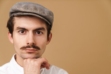 Image closeup of serious mustached man wearing hat looking at camera and touching his chin
