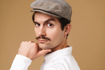 Image closeup of confident mustached man wearing hat looking at camera and touching his chin