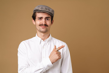 Image closeup of displeased mustached man wearing hat pointing finger at copyspace