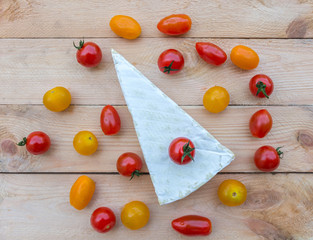 Cheese and colorful red, orange and yellow cherry tomatoes on wooden background. 