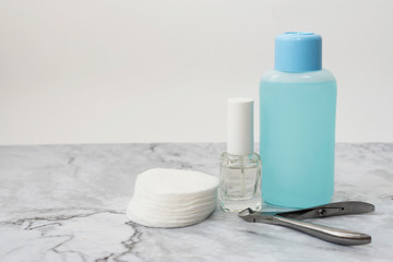 Set of manucure nail care products on a soft marble surface. Glass bottle with colorless firming nail polish, plastic bottle with nail varnish remover and cotton pads. Front view. Copy space for text