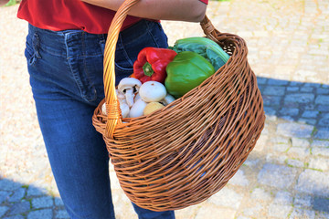 a woman, a housewife, wearing dark blue jeans and a red blouse, holds a wicker basket full of loose vegetables, concept of limiting the amount of plastic packaging in everyday life