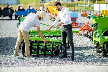 Young agronomist with salesman or manager at the open ground of the shop with agricultural...