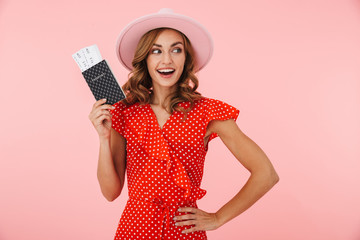 Naklejka premium Young woman tourist posing isolated over pink wall background holding passport with tickets make winner gesture.