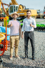 Young agronomist with salesman at the open ground of the shop with agricultural machinery, buying a new planter for farming