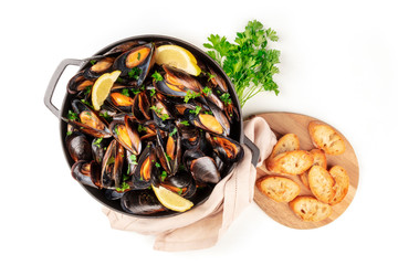 Marinara mussels, moules mariniere, overhead shot in a cooking pan with toasted bread and fresh parsley on a white background with copyspace