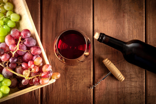 Cellar Tasting. A photo of a red wine glass with a bottle, grapes, and a vintage corkscew, shot from the top on a dark rustic wooden background