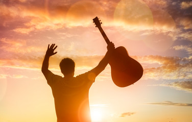 Silhouette of guitarist musician holding guitar against sunset