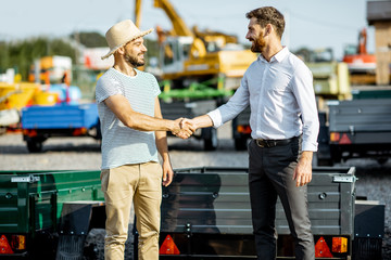 Agronomist shaking hand with salesman, buying a new farm truck trailer on the open ground of the...