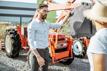 Agronomist choosing a tractor for farming, standing with salesman on the open ground of...