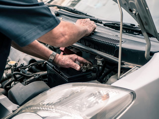 Old man auto mechanic replace a new battery into a car