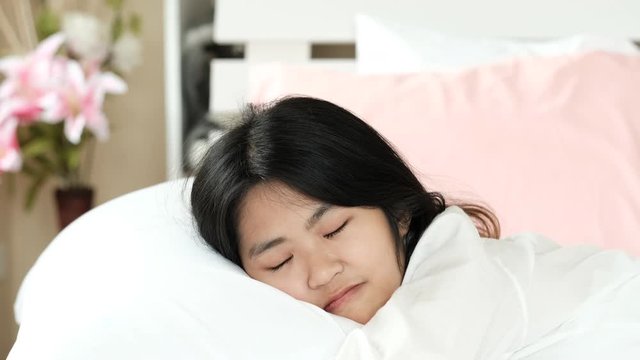 Asian pretty teen girl wake up and smile on white bed and look happy with her dream.