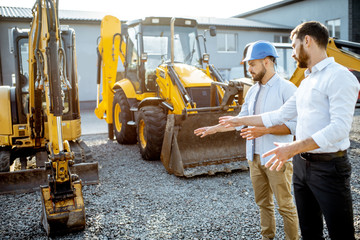 Builder choosing heavy machinery for construction with a sales consultant on the open ground of a...