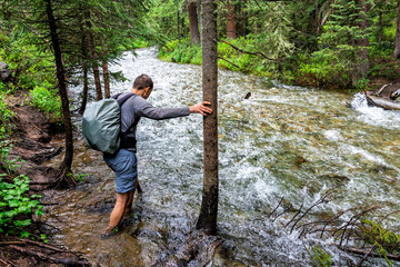 Man crossing river ford on Conundrum Creek Trail in Aspen, Colorado in 2019 summer in forest woods with strong current