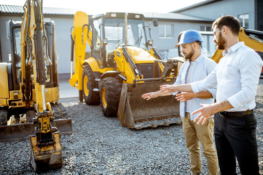 Builder choosing heavy machinery for construction with a sales consultant on the open ground of a shop with special vehicles