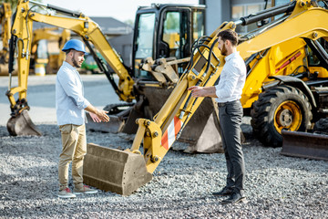 Builder choosing heavy machinery for construction with a sales consultant on the open ground of a...