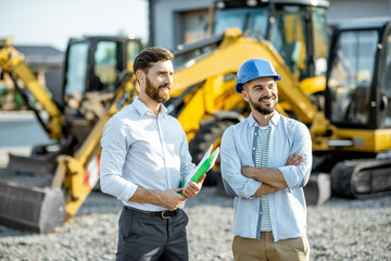 Builder choosing heavy machinery for construction with a sales consultant standing with some...